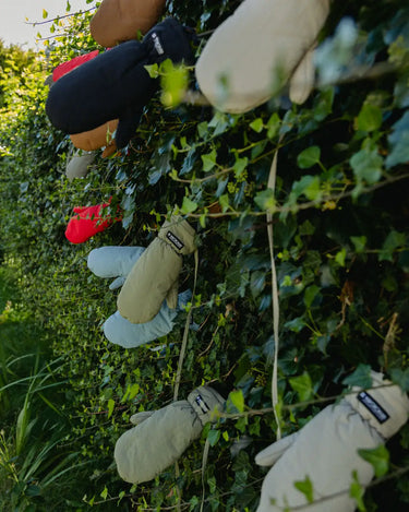 Set of vegan winter gloves in cinnamon, beige, gray, and black made from recycled materials hanging outdoors on a leafy wall. - The New Orchard - ⁠Fresh Cinnamon