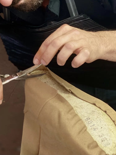 Person cutting a beige vegan shoe with scissors, focusing on the action.
