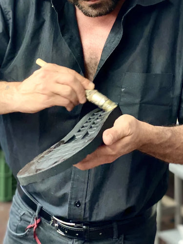 Man working on a shoe with a tool, wearing a black shirt.